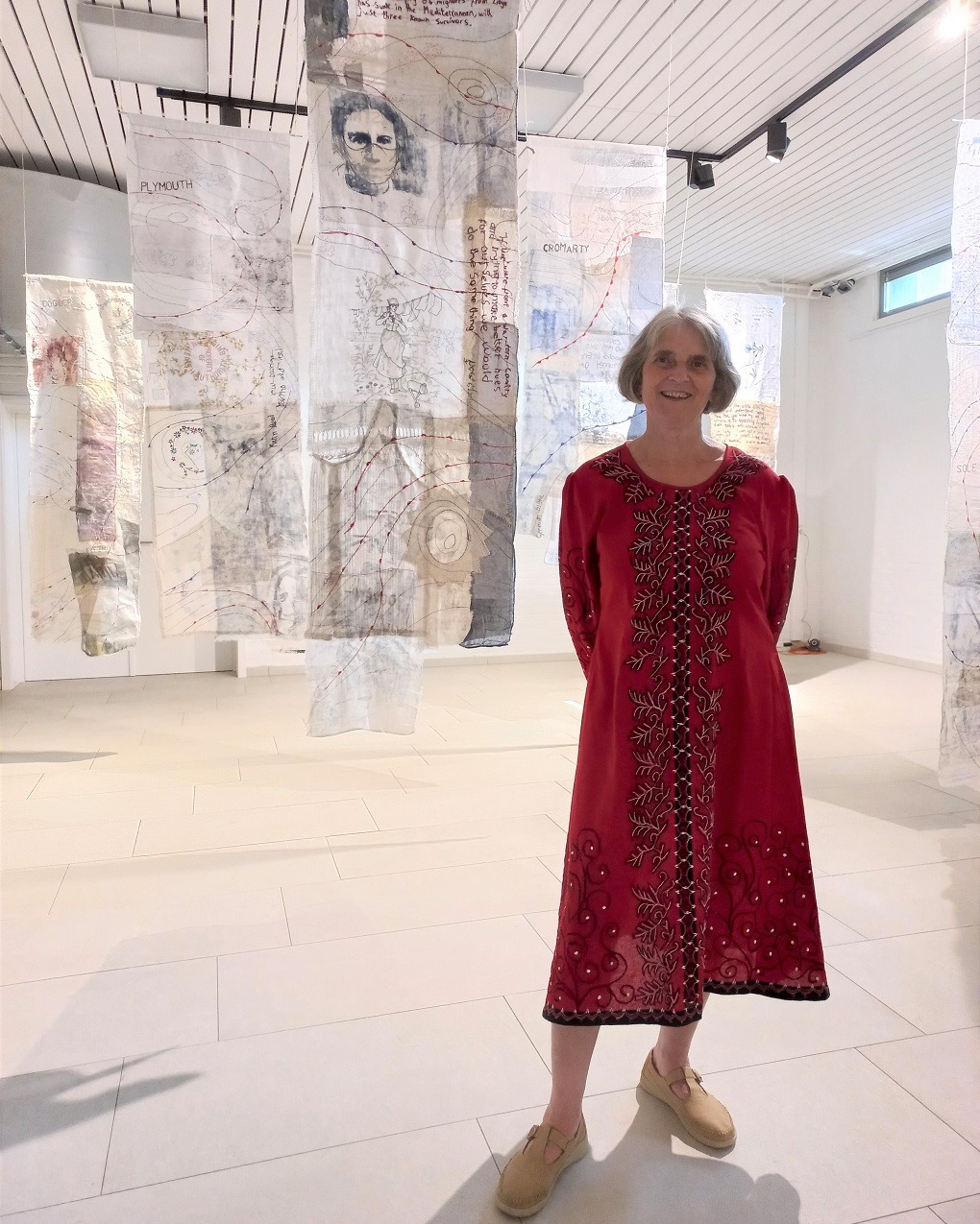 Textile Artist Cas Holmes standing at her exhibition in front of her work